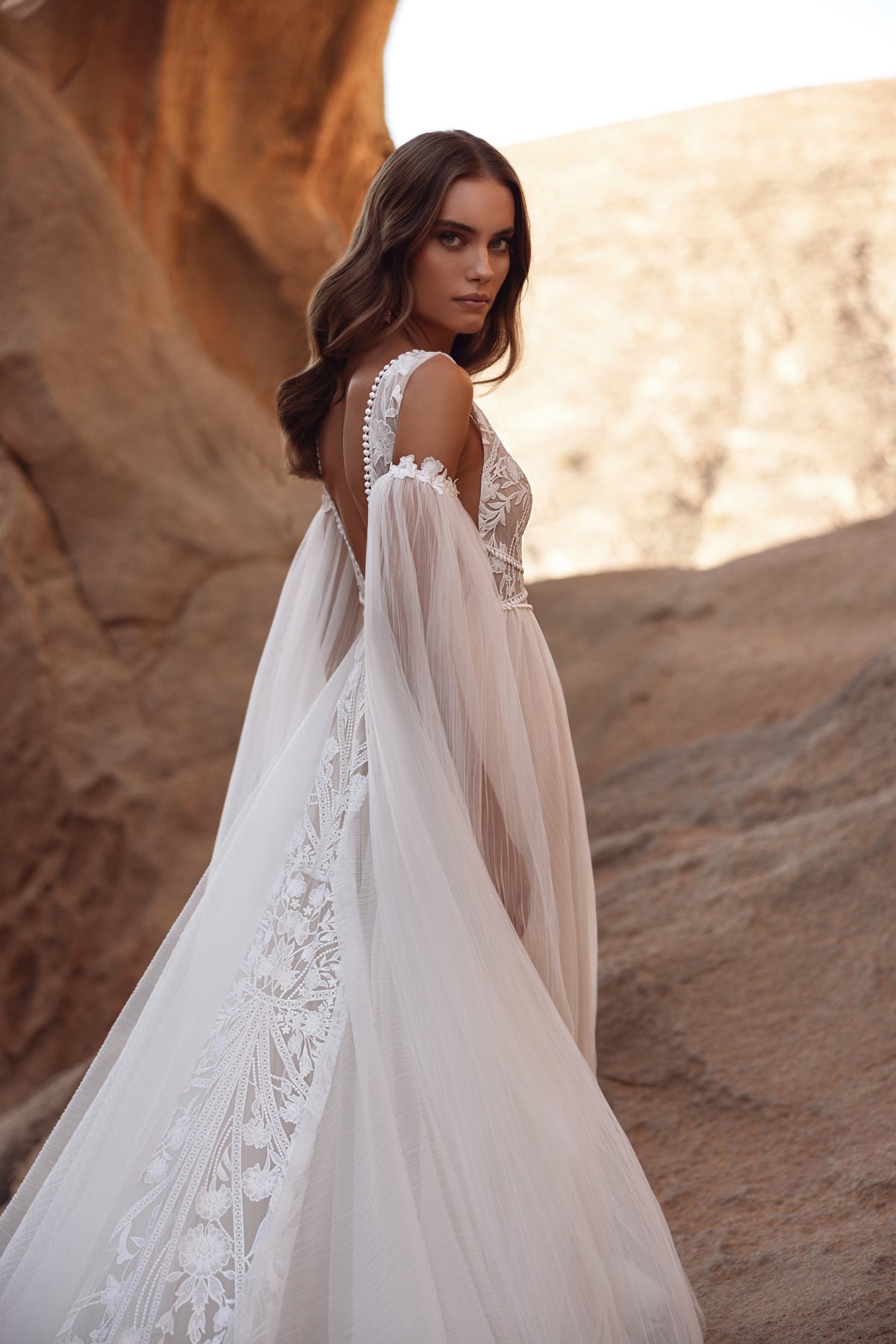 Three-quarter back view of Salome wedding dress, with boho lace and flowing sleeves in the wind