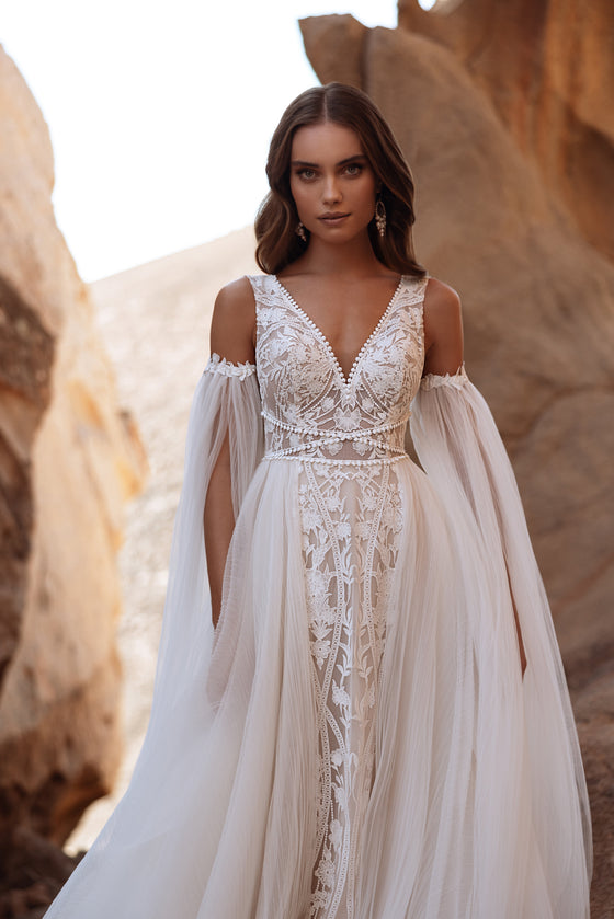 The Salome off-the-shoulder wedding dress with long tulle sleeves blends boho charm with romantic lace detailing.