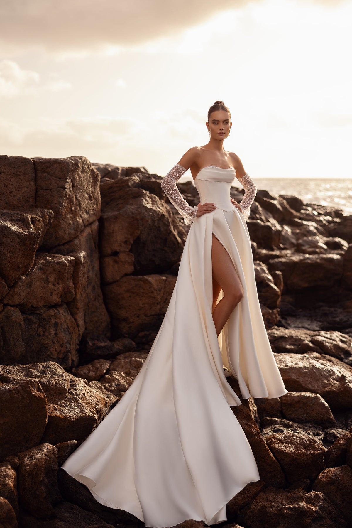 Full-length Sarabi wedding dress by the sea, showing the wide satin skirt and slit