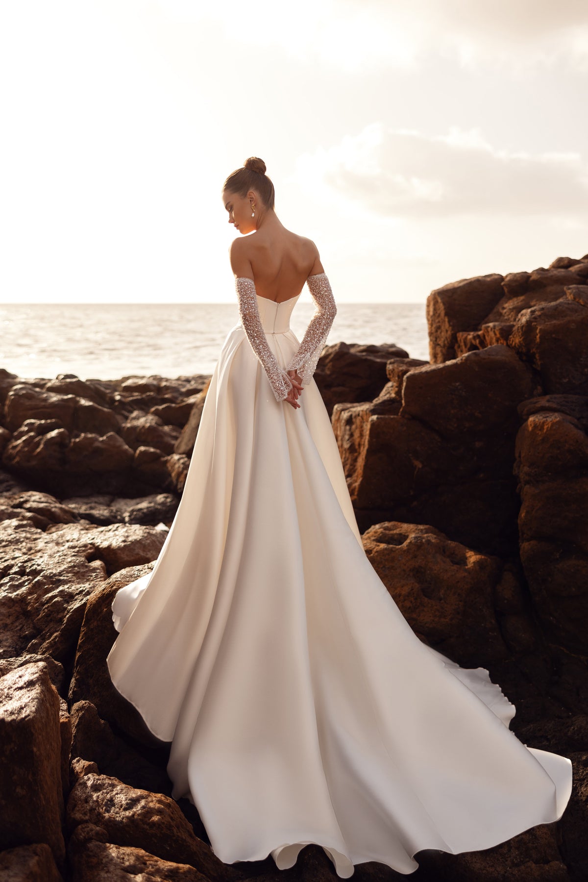 Sarabi wedding dress from behind on the rocks, with its satin train spread across the stone