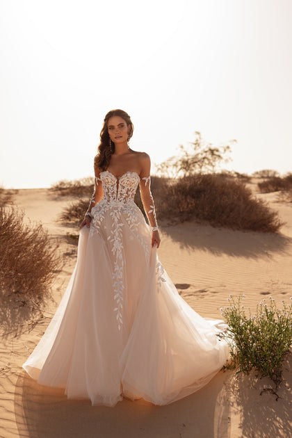 The Tamara bridal gown featuring an off-the-shoulder corset and soft tulle train embodies timeless desert elegance.