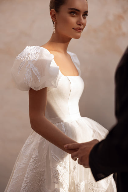 The Vanilla bridal dress with voluminous skirt and floral lace details offers timeless bridal romance.
