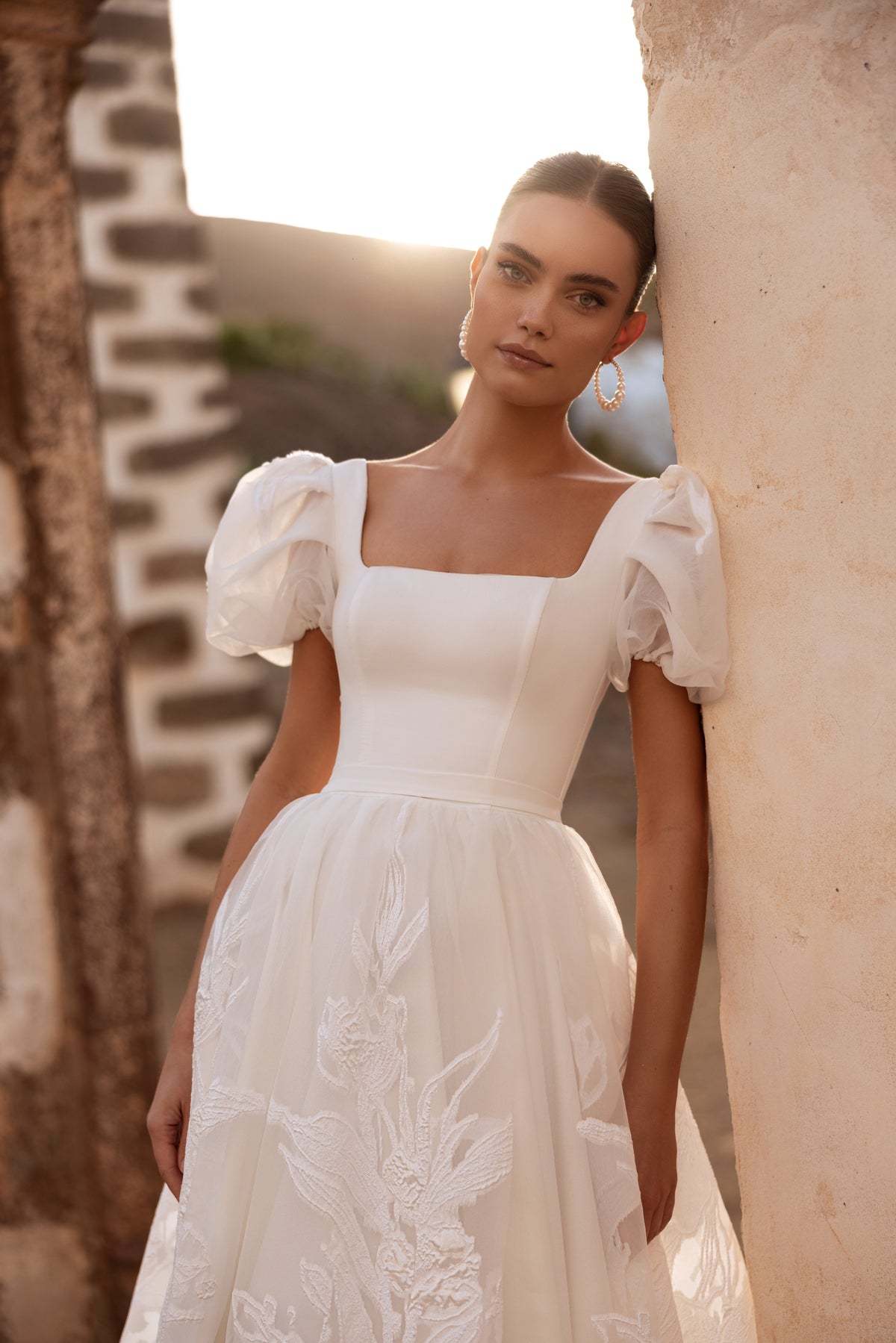 Vanilla wedding dress beside a stone wall, with puff sleeves and a square neckline